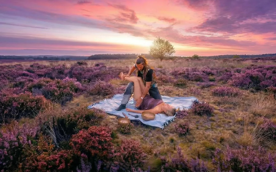 Massage with singing bowls on a blanket in the blooming heather at sunset