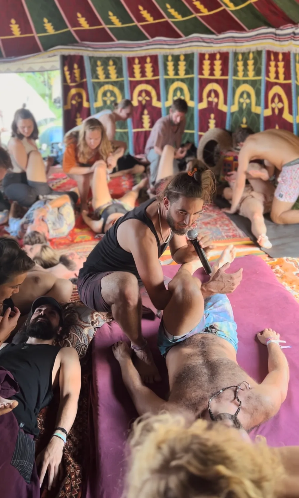 Michalis geeft uitleg met een microfoon tijdens een massageworkshop in een festivaltent